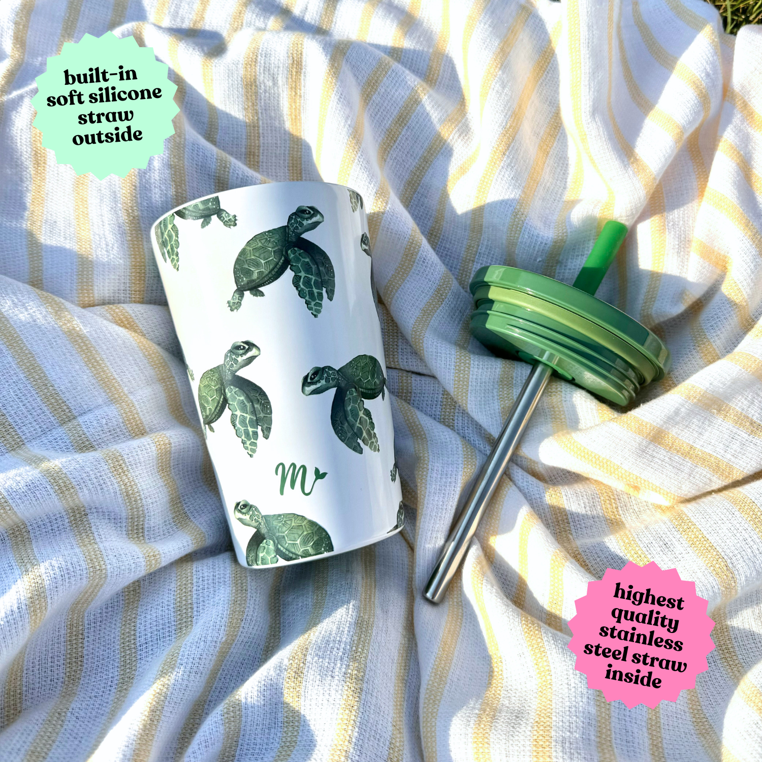 14 oz stainless steel cup with a sea turtle design placed on a striped cloth, with the lid and stainless steel straw set beside it, showcasing the cup's removable components.